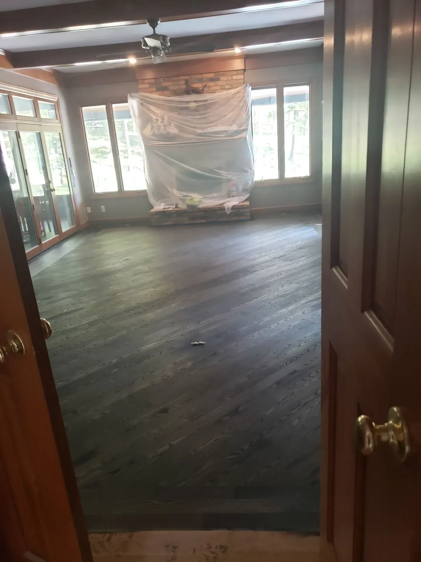 View of a room with dark wood flooring, windows, and a fireplace covered in plastic.