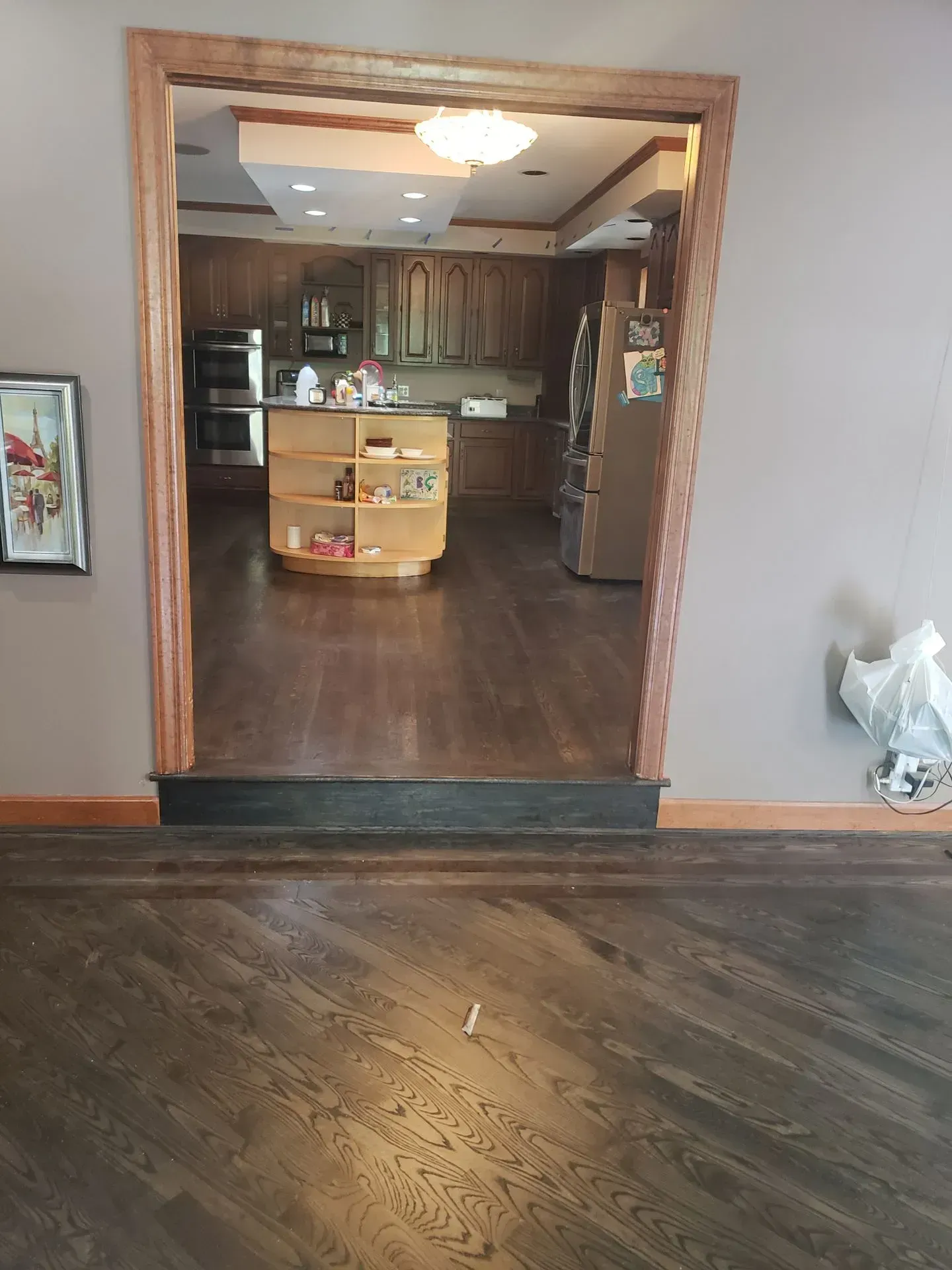 View of a kitchen from an adjacent room. Dark hardwood floors lead to the kitchen. A wooden island is visible.