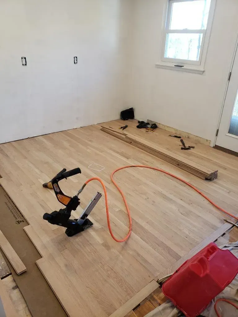 Hardwood floor installation in a room with tools and materials scattered about.