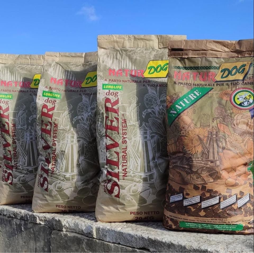 Confezioni di cibo per cani in sacchetti allineate all'aperto su una sporgenza rocciosa, sotto un cielo azzurro.