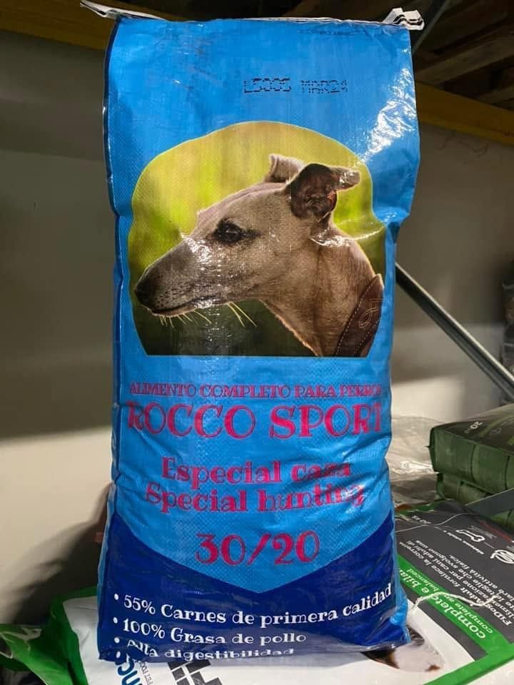 Sacchetto di cibo per animali blu e verde con la foto di un cane e testo rosso, posizionato verticalmente su uno scaffale.