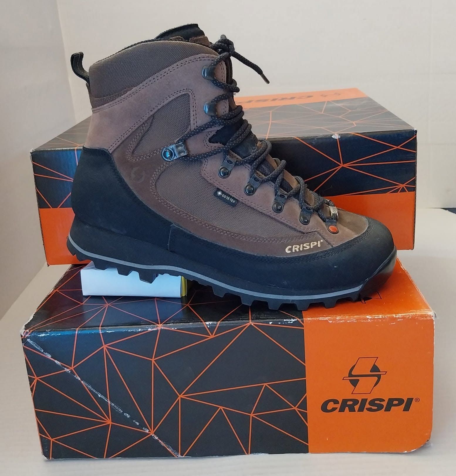 Scarponcino da trekking Crispi marrone e nero su scatole da scarpe arancioni e nere