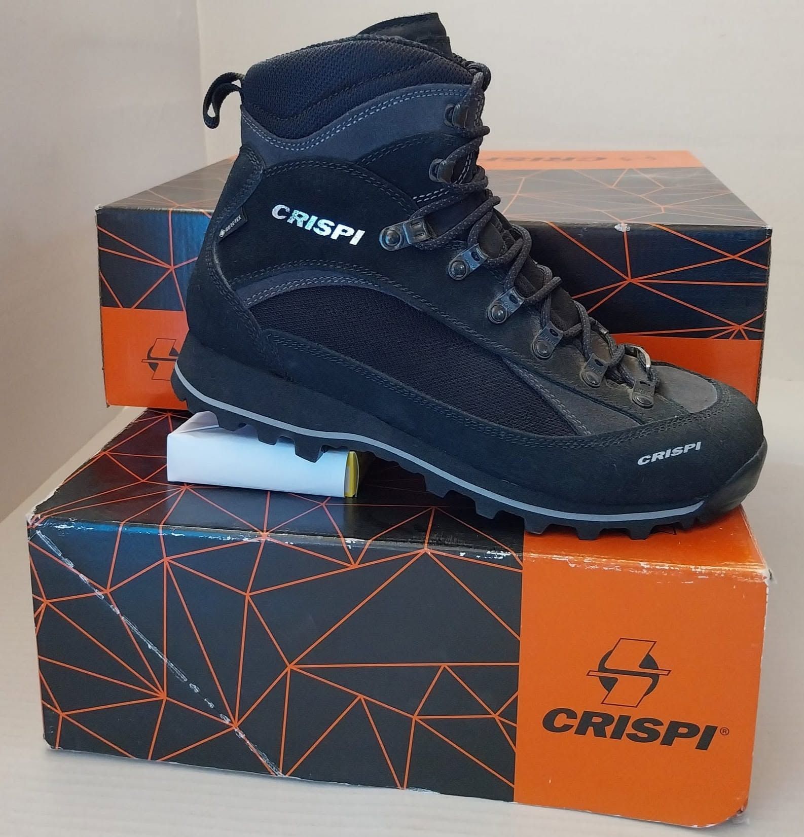 Scarponcino da trekking Crispi nero esposto su una scatola da scarpe arancione e nera.