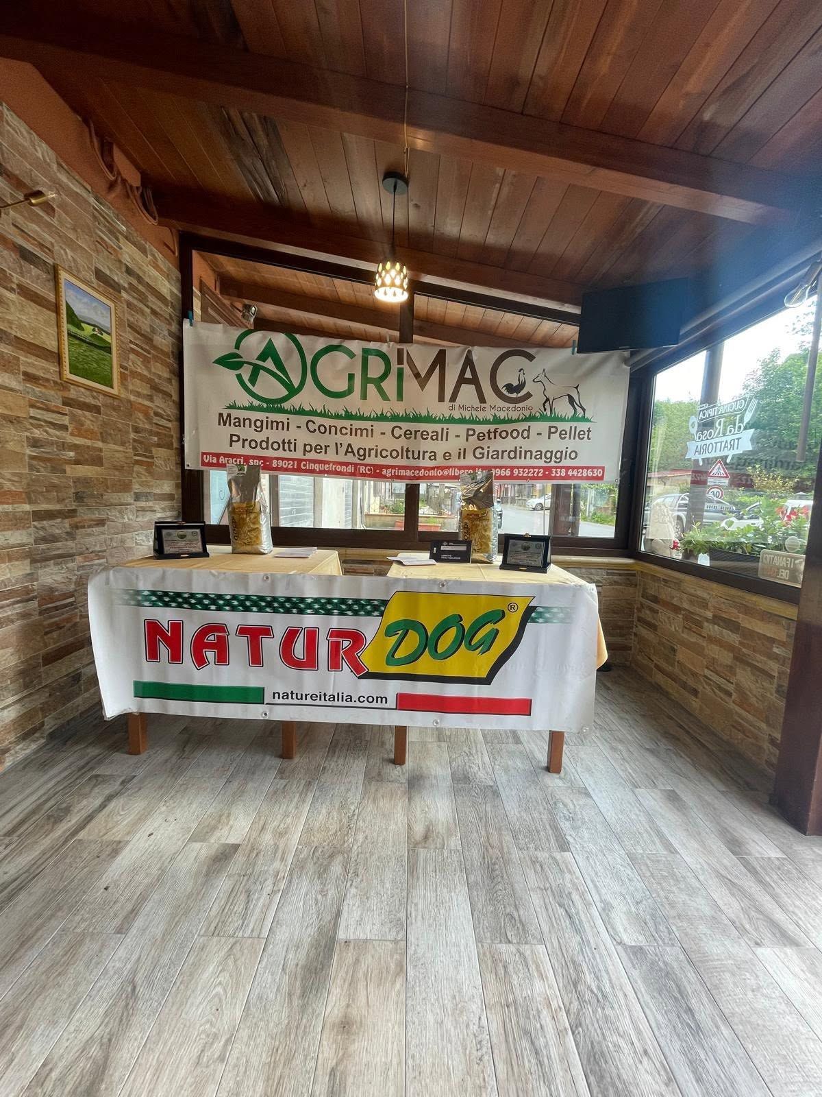 Stand rustico al coperto con striscioni AGRIMAC e NATUR200 sotto un tetto di legno.
