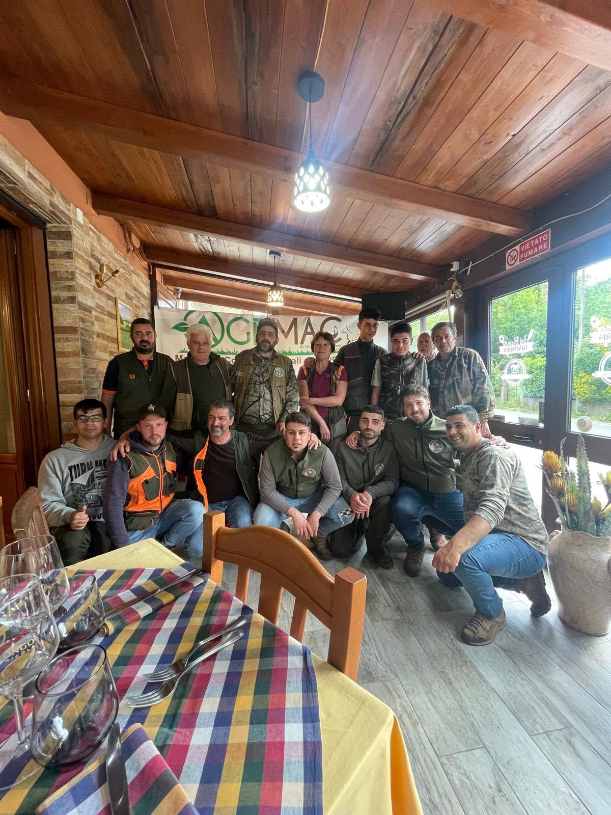 Gruppo di persone in posa all'interno di una stanza rustica in legno con una tovaglia a quadri in primo piano.