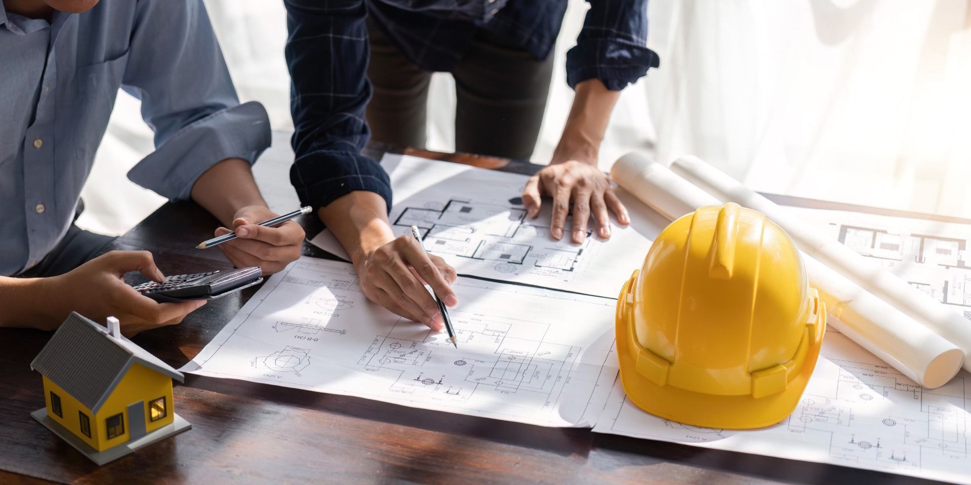 Two people reviewing blueprints with a yellow hard hat and model house on a table.