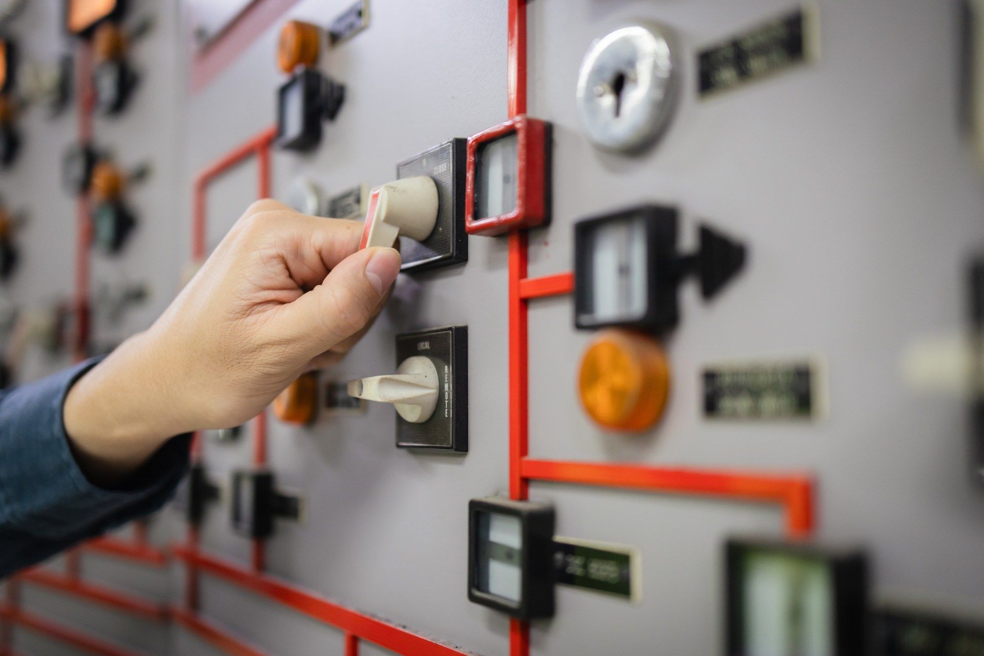 Hand turning a switch on a control panel with red piping and various gauges.
