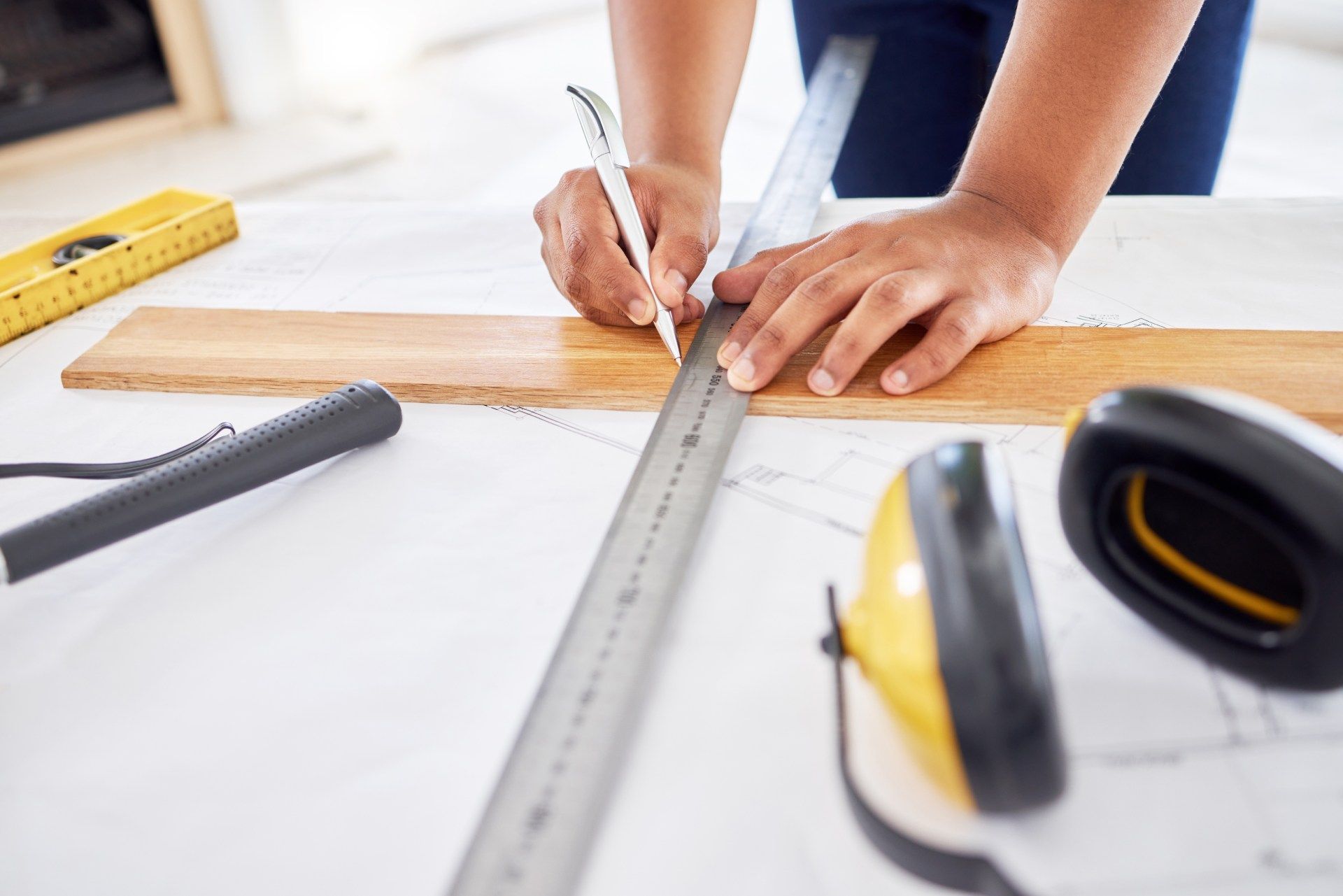 Person using a ruler and pencil to measure and mark wood on a white surface with tools.