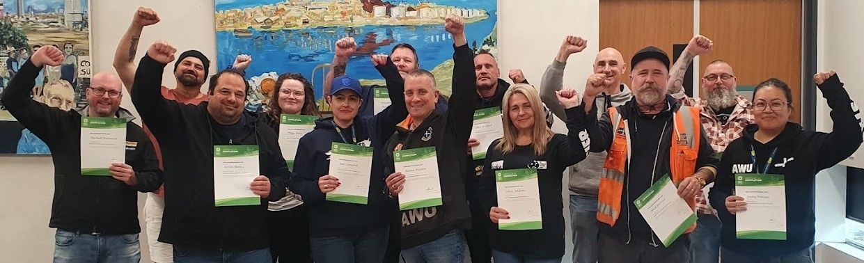Group of runners posing indoors with medals and certificates, smiling and raising their arms in celebration