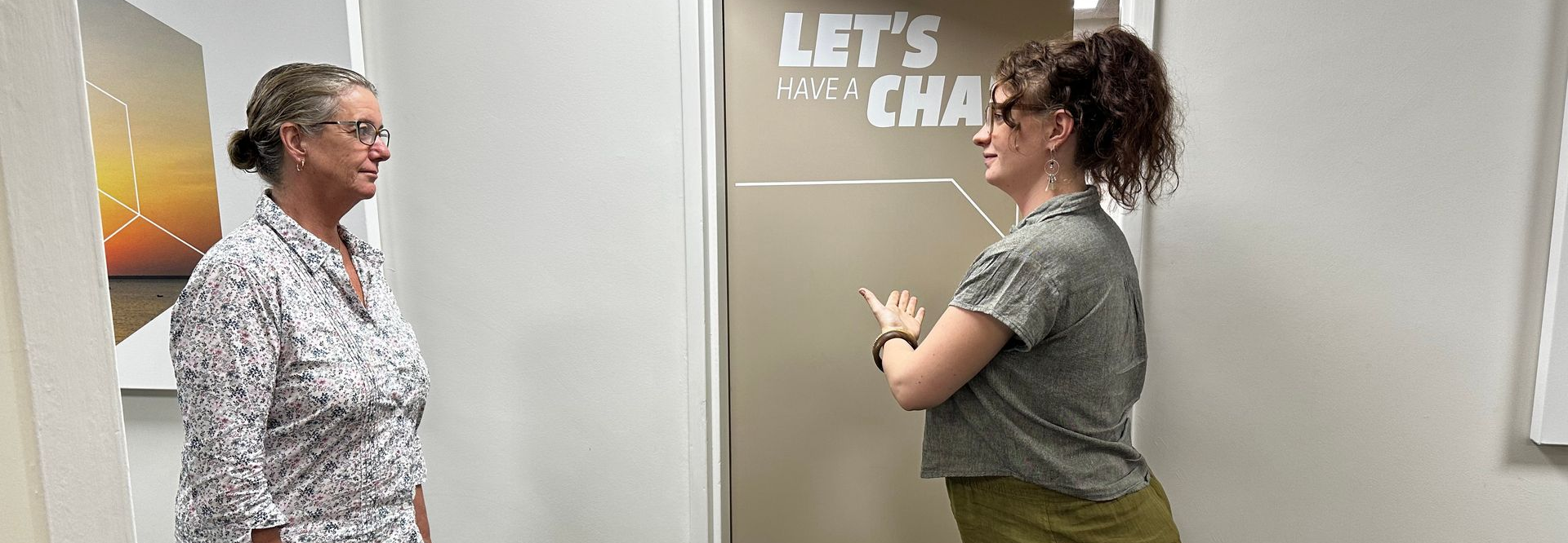 Two people facing each other near a wall with the words “LET’S CHAT” between them.