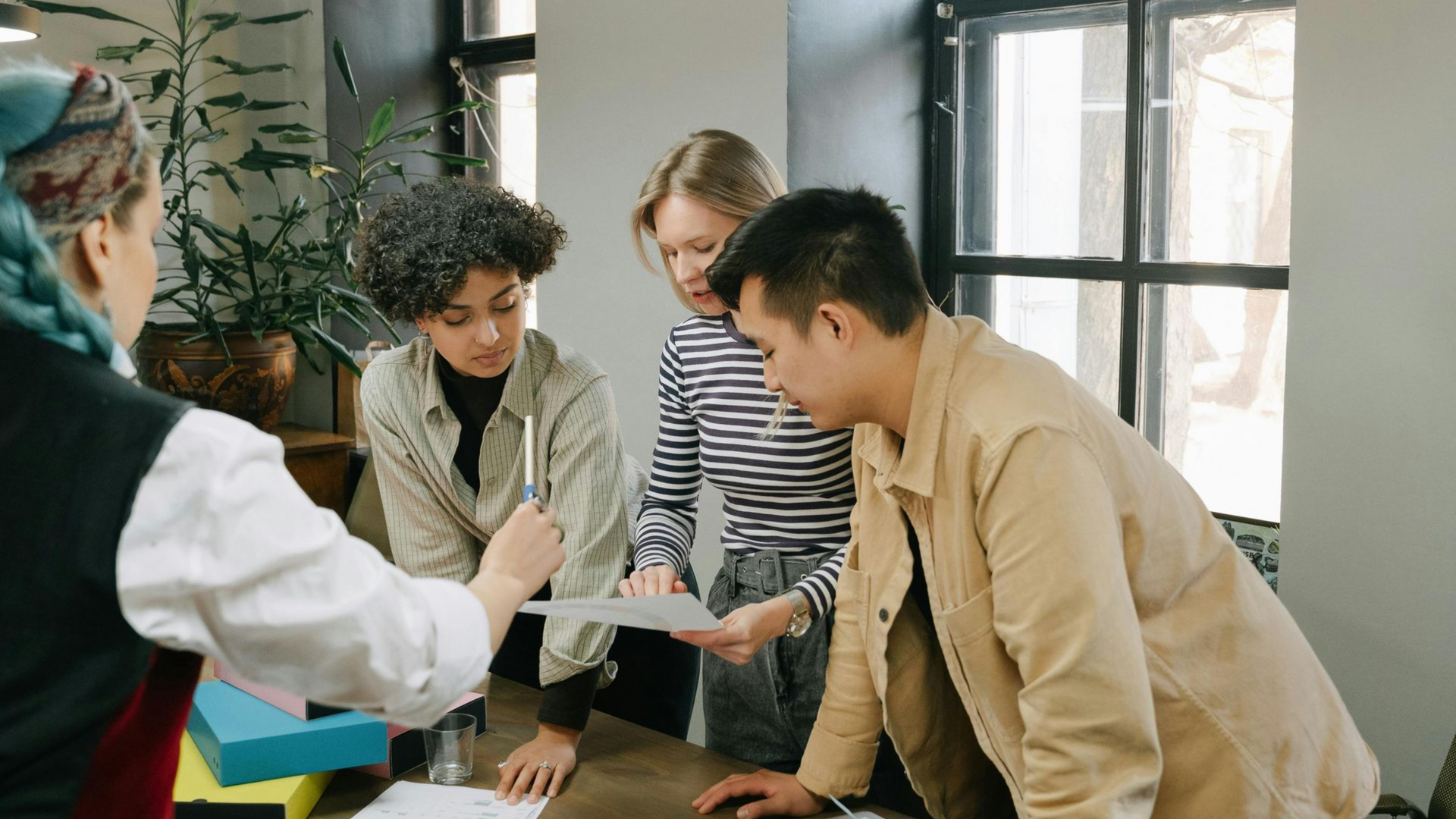 Group of people gathered around a table, leaning in and discussing documents in a bright office