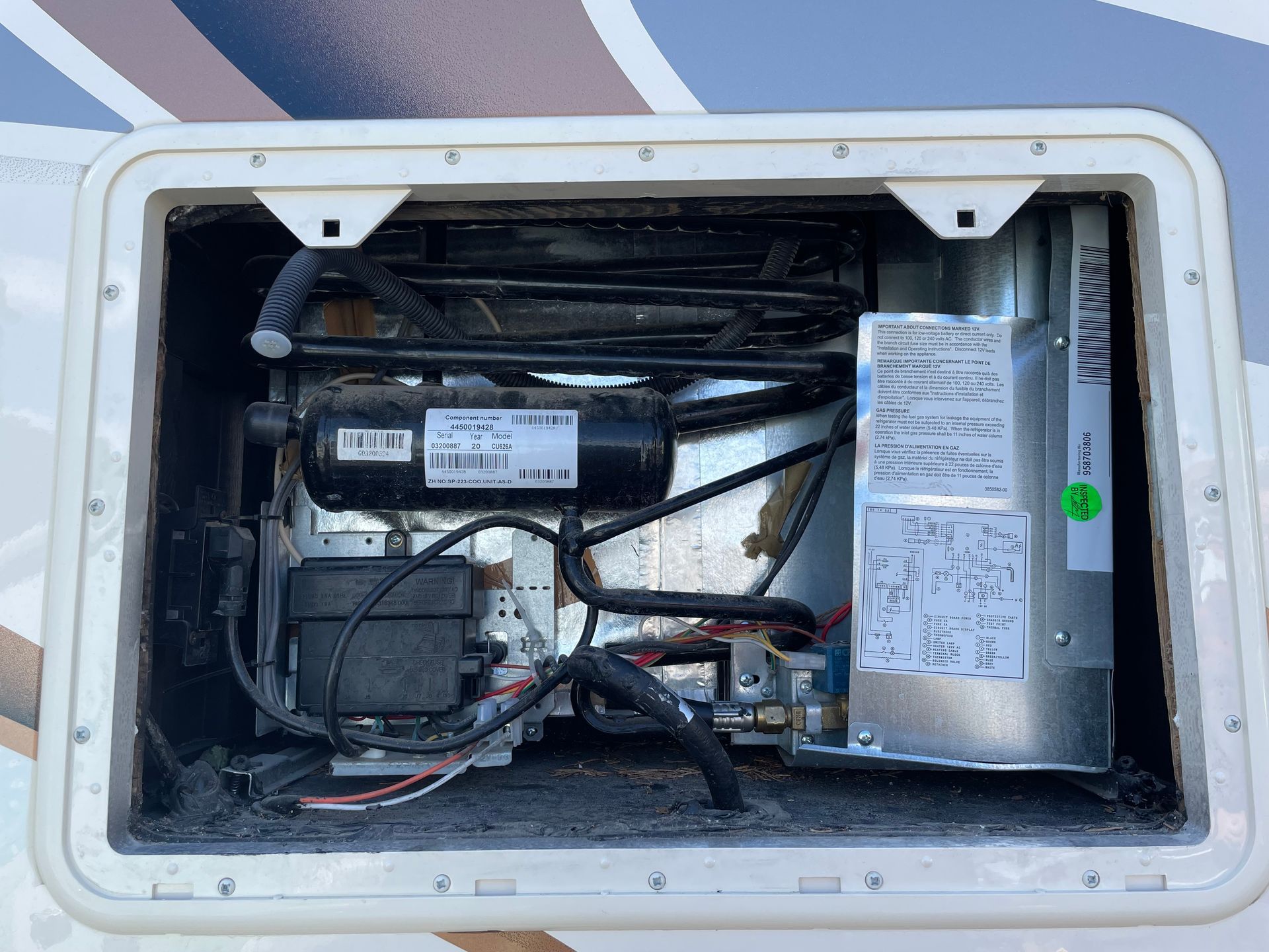 RV refrigerator exterior, revealing internal components: compressor, wiring, and control panel.