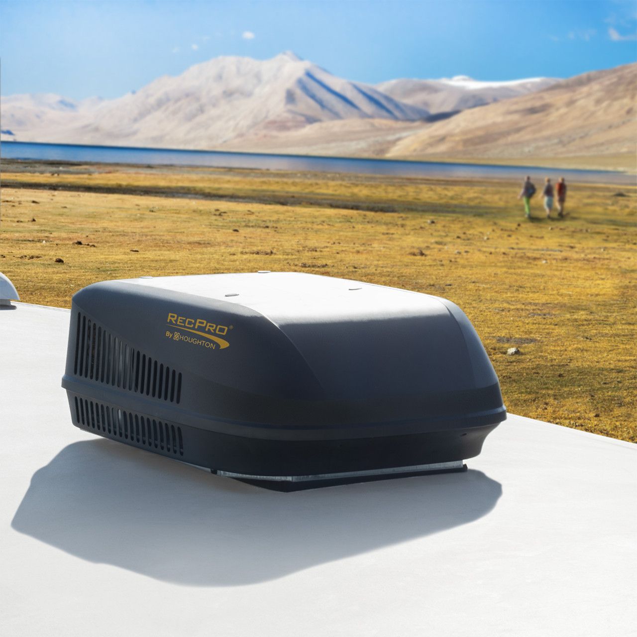 Black RV air conditioner on a white roof, with a scenic mountain and lake backdrop. Three people walk in the distance.