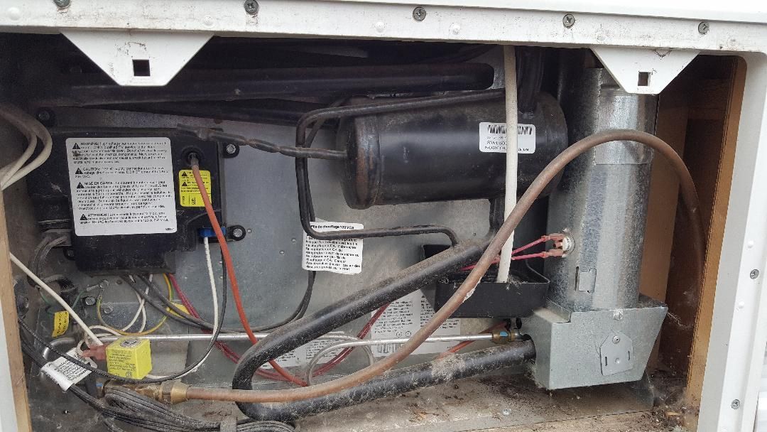 Close-up view of a RV refrigerator’s mechanical components with a black motor, wiring
