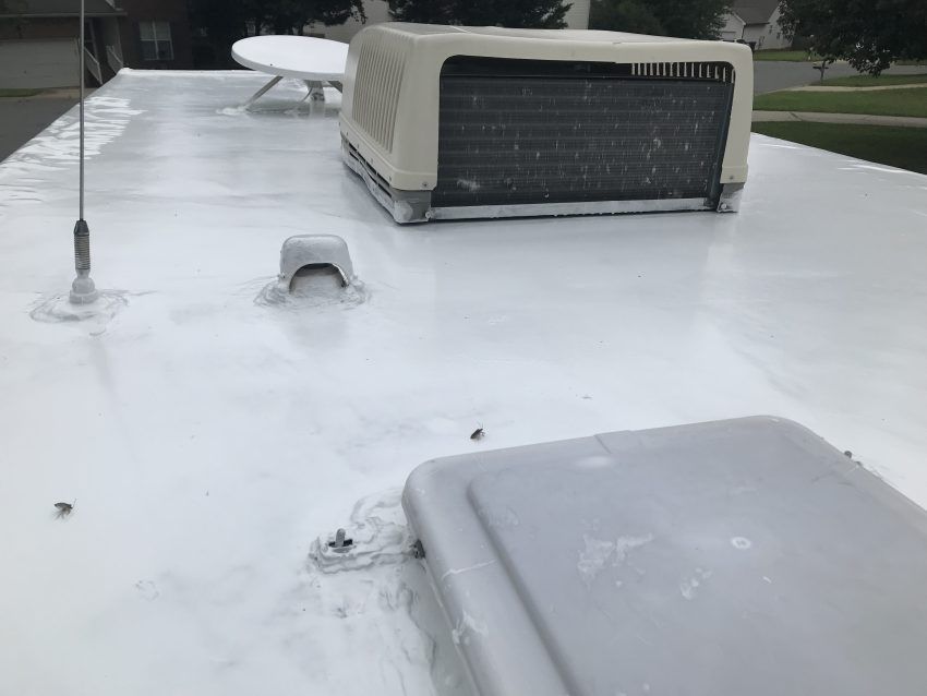 White RV roof with air conditioner, antenna, and satellite dish.  The roof is painted with a white sealant.