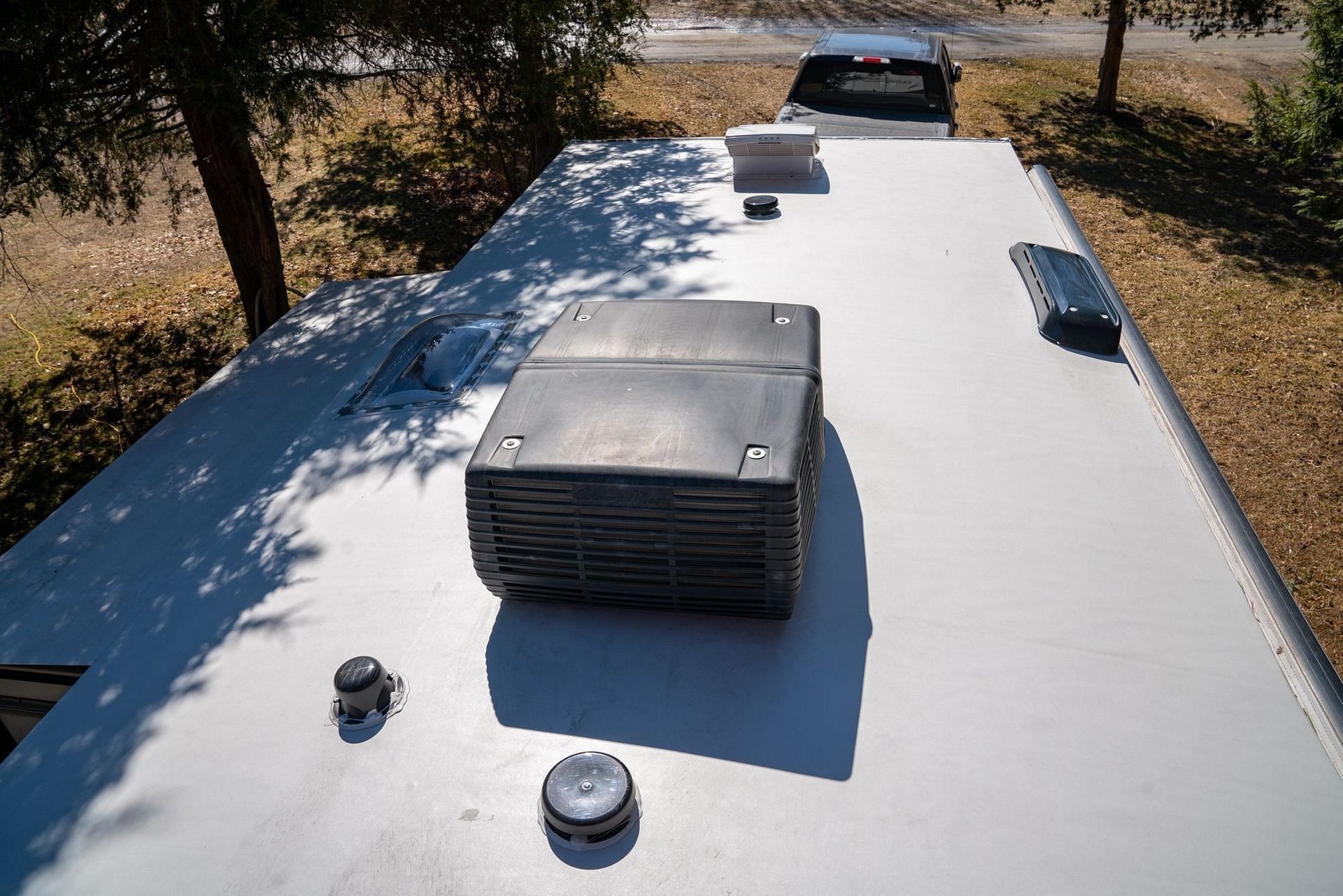 View of the roof of an RV, featuring air conditioning unit, vents, and a parked vehicle in the background.