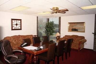 A professional conference room with a long wood table, leather chairs, two patterned sofas, a ceiling fan, and decor.