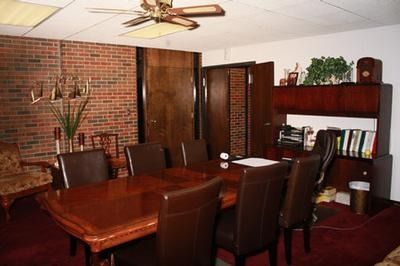 A wood-paneled conference room features a dark wood table with brown leather chairs on a maroon carpet.