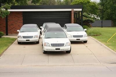 Three white limousines and hearses parked in a residential concrete driveway in front of a modern garage.