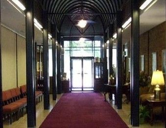 A symmetrical interior hallway leads to a glass doorway. It features a maroon carpet, black pillars, and arched ceilings.