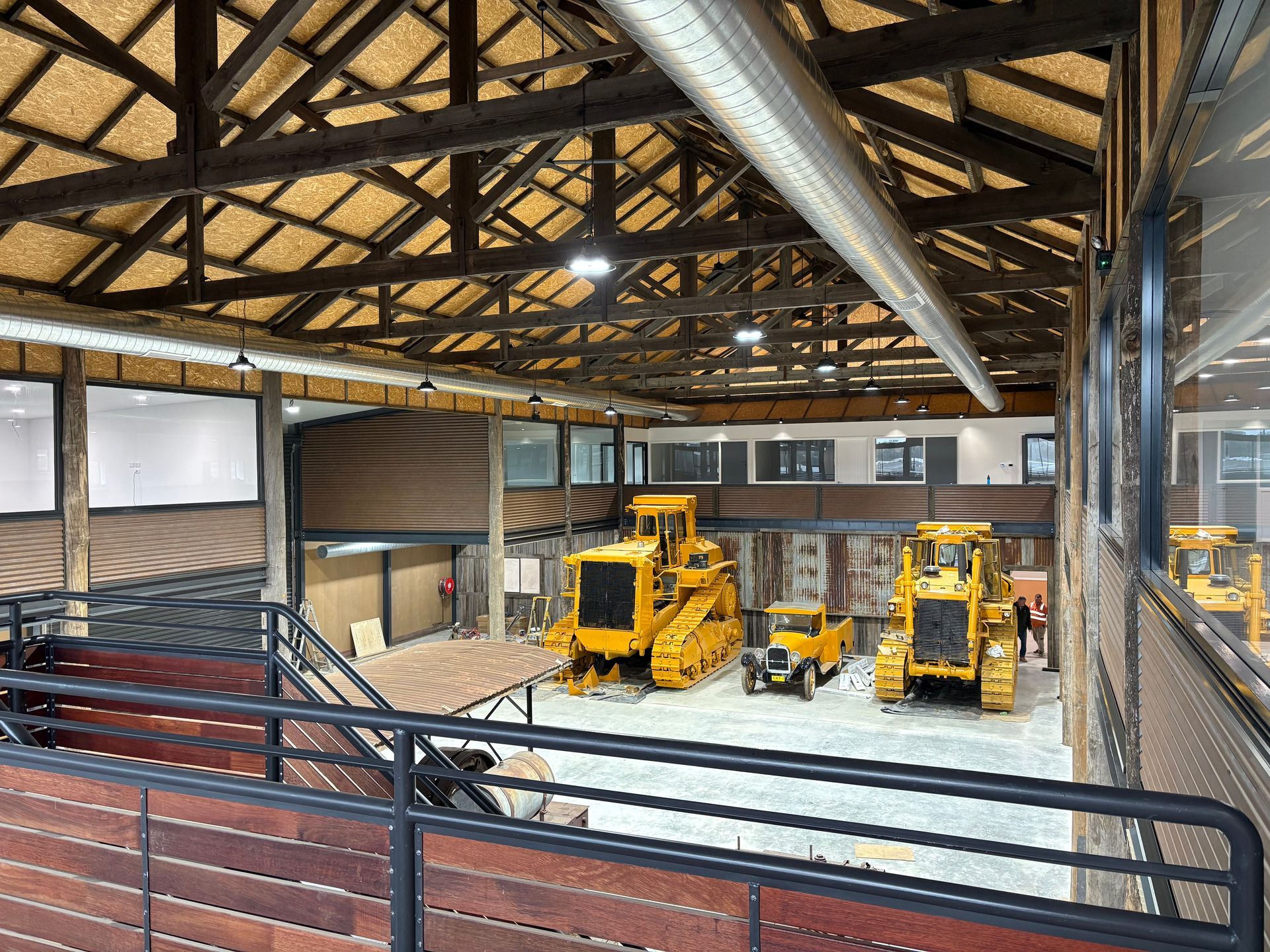 Inside view of a large barn exhibiting yellow construction equipment; wooden beams, metal railings — SJD Electrical Contracting in Cowra, NSW