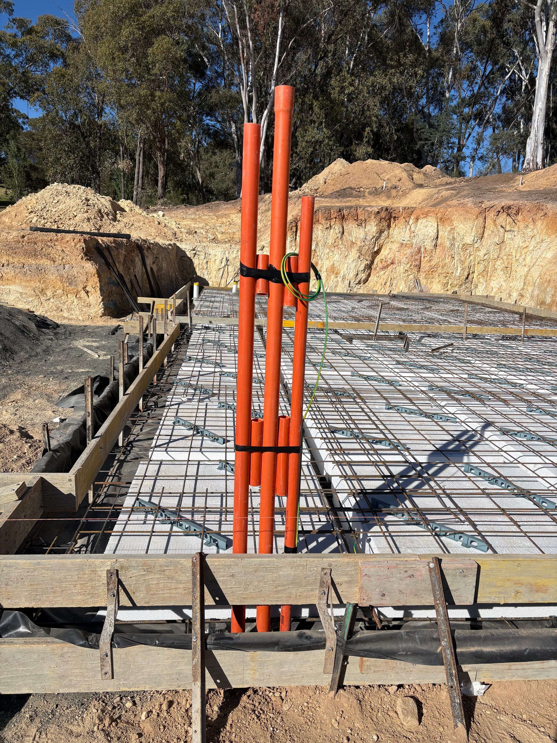 Orange conduits bundled on concrete foundation framework at a construction site.