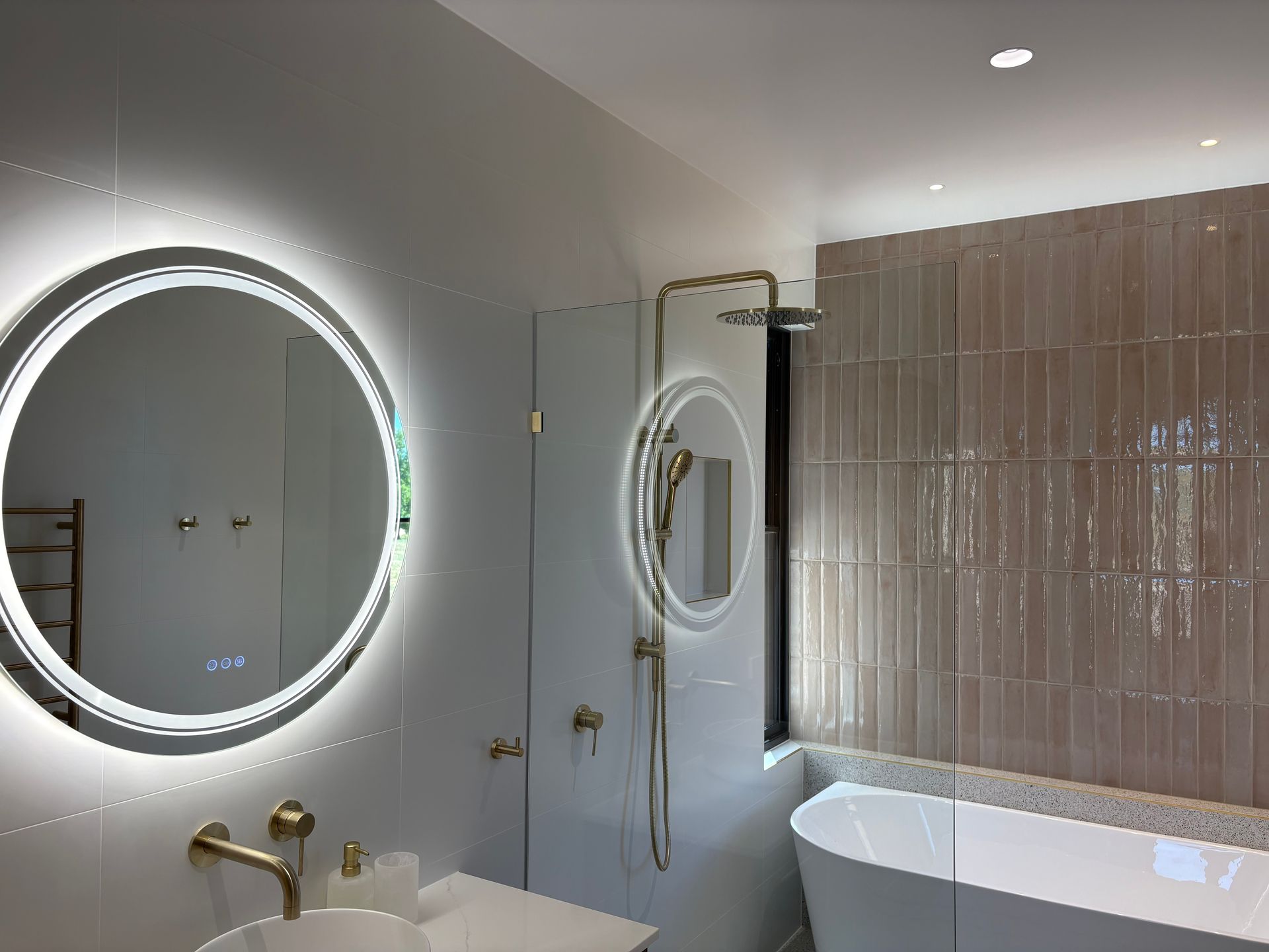 Modern bathroom with a round mirror, gold fixtures, and tiled wall above a bathtub — SJD Electrical Contracting in Parkes, NSW