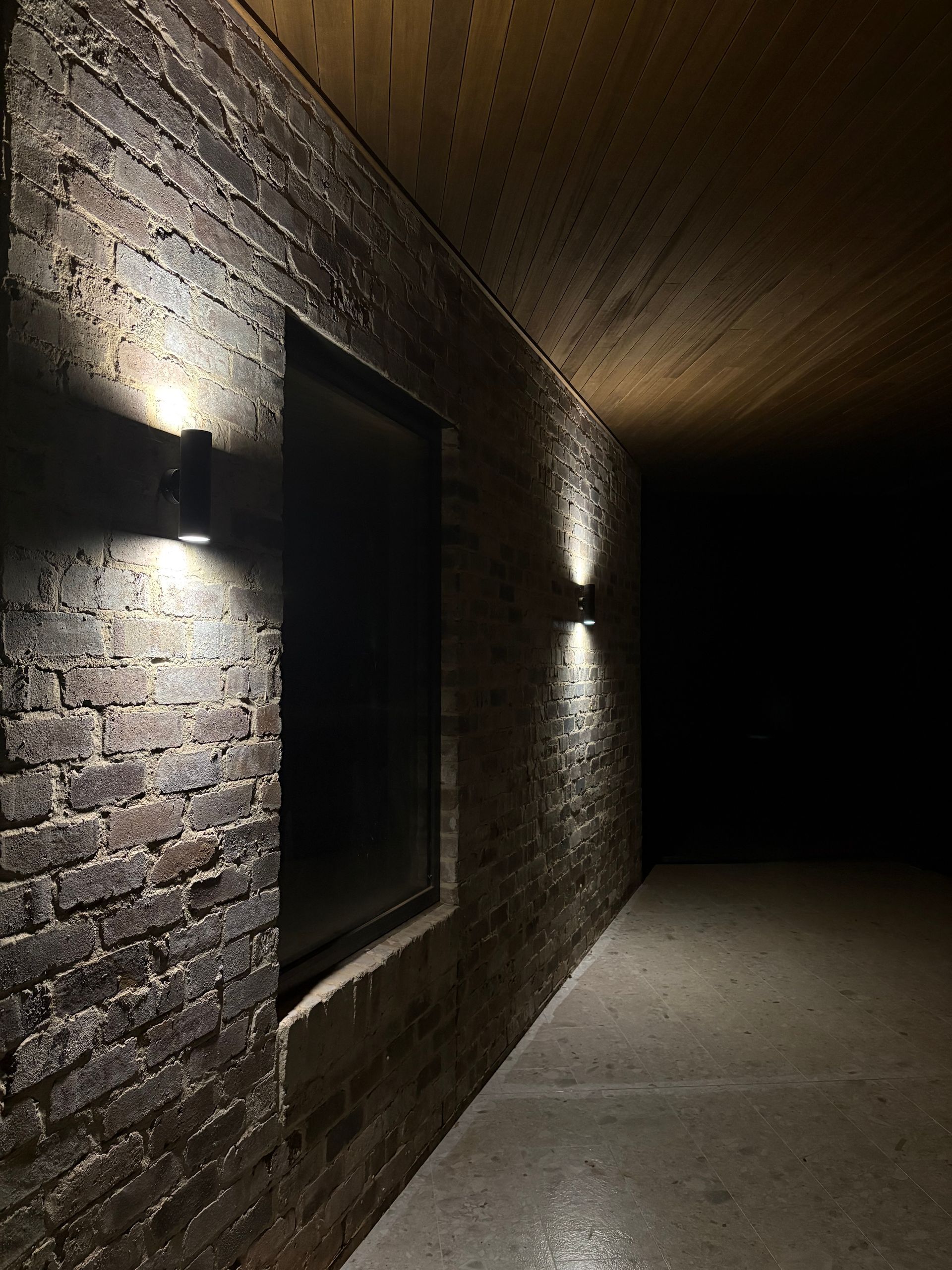 Brick wall with two outdoor lights, a window, and a dark corridor — SJD Electrical Contracting in Forbes, NSW