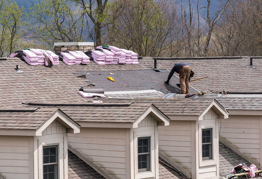 Roofing contractor removing the old tiles before replacing with new shingles on a townhouse roof 