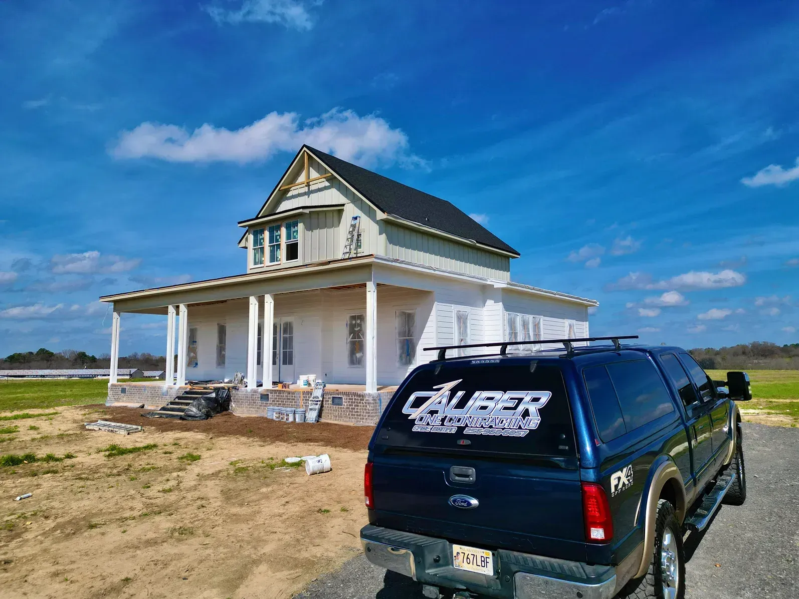 White house under construction beside a black pickup truck in a sandy rural area under a bright blue sky