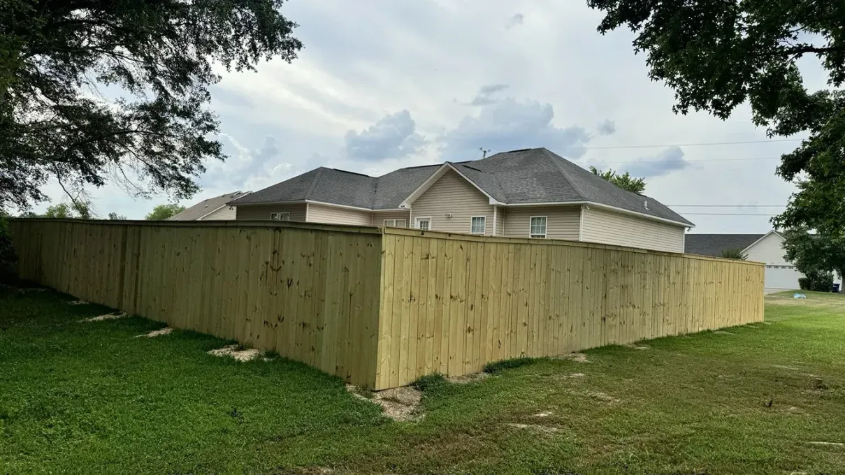 Large wooden privacy fence surrounds a backyard behind a suburban house on a cloudy day