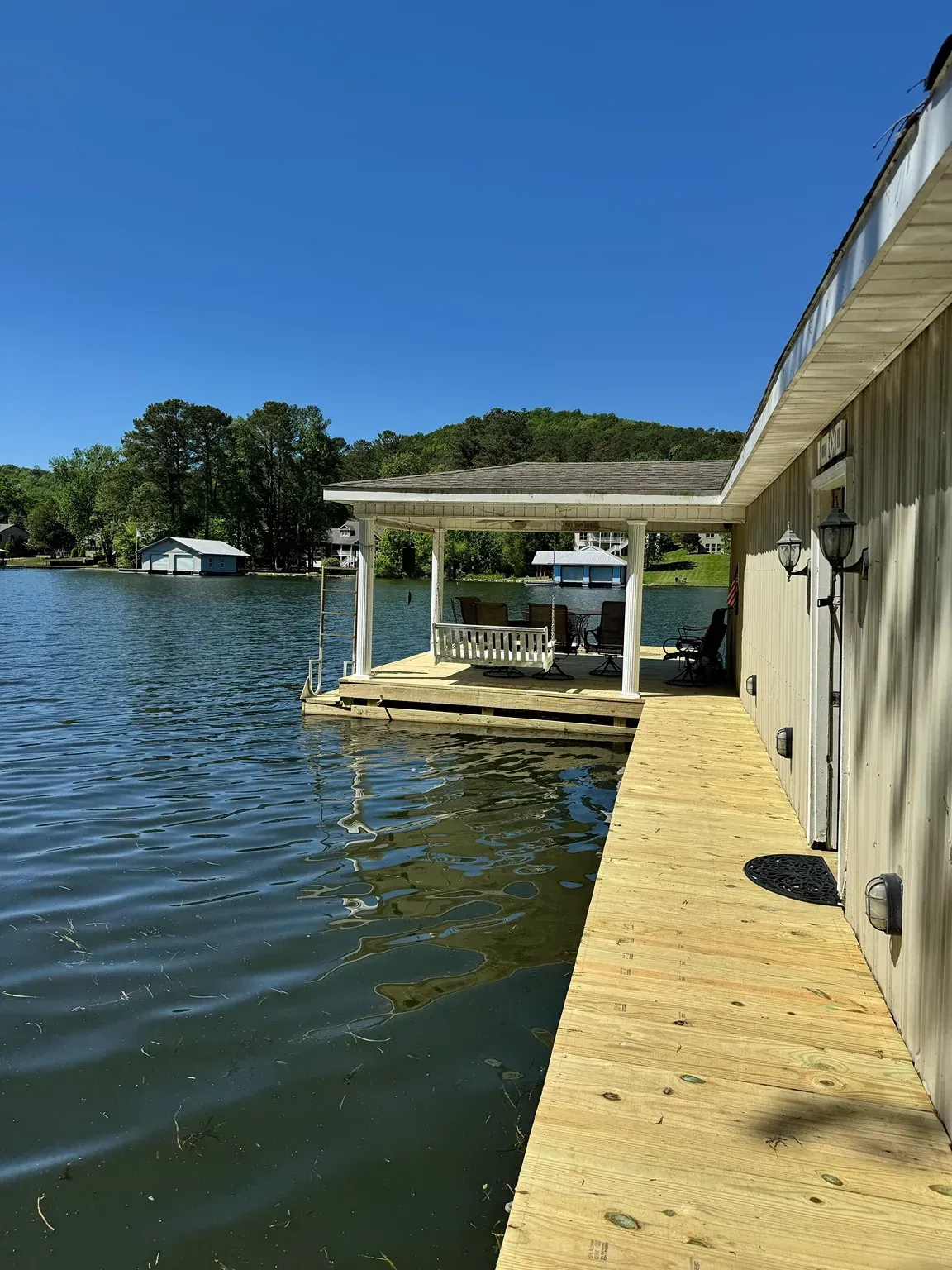 Dock beside a calm lake, with a wooden walkway and covered boat lift under a clear blue sky.