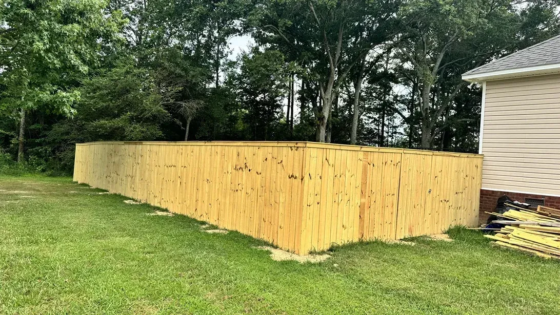 Yellow wooden fence enclosing a grassy yard beside a house, with trees in the background