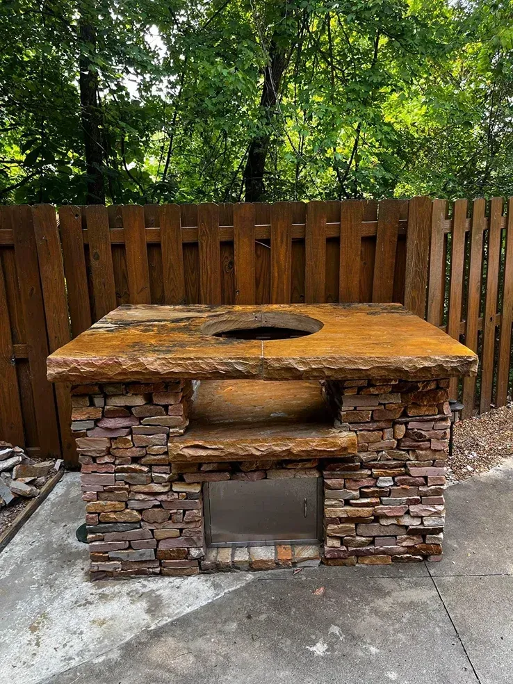 Brick outdoor grill with stone countertop and wooden fence in a backyard yard