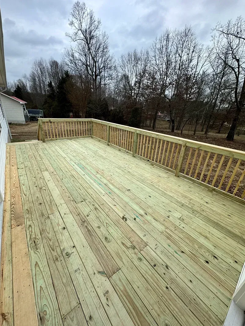 New wooden deck under construction beside a house, with railings and bare trees in the background