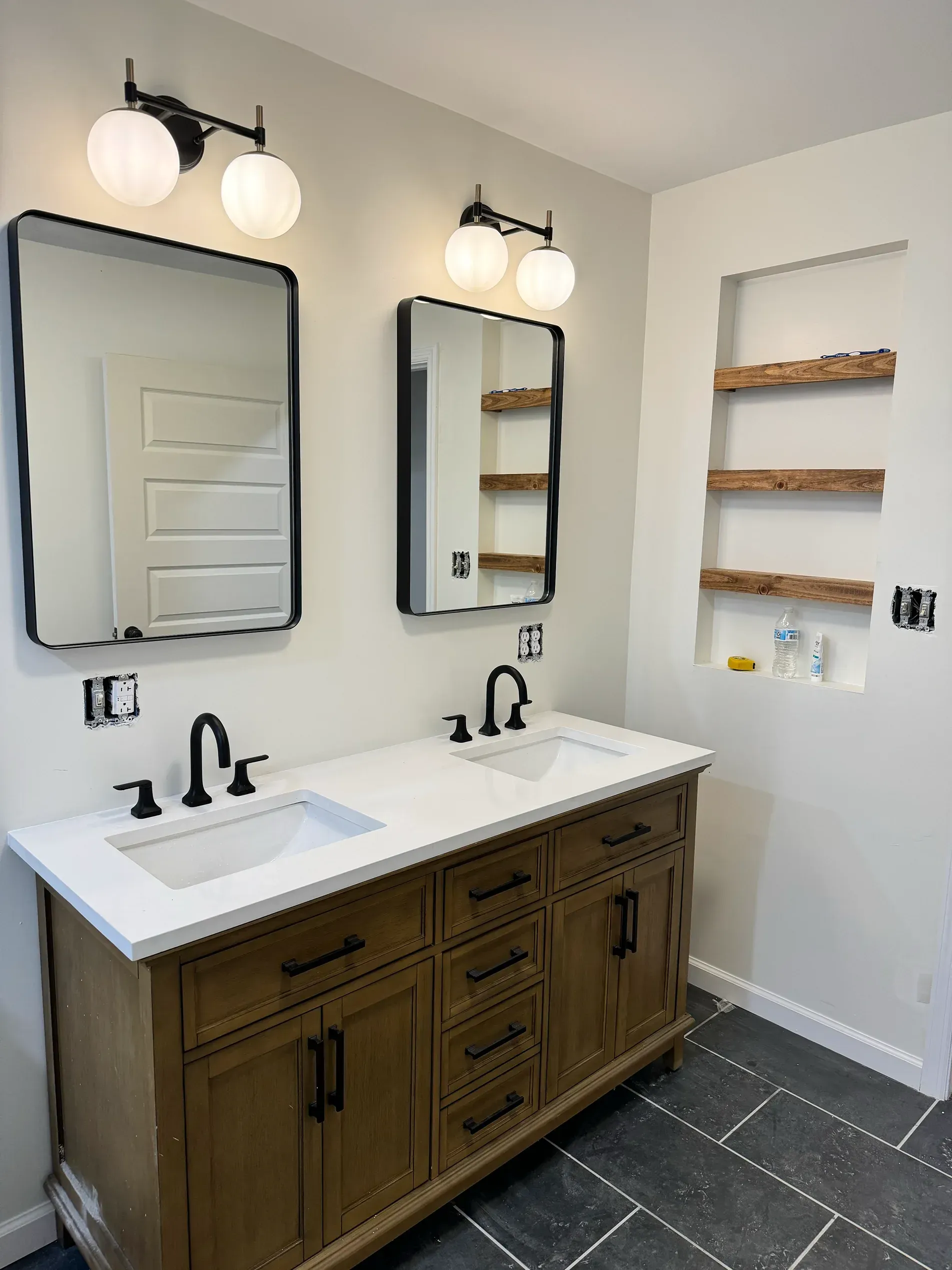 Modern double-sink bathroom vanity with dark wood cabinets, black mirrors, and wall sconces