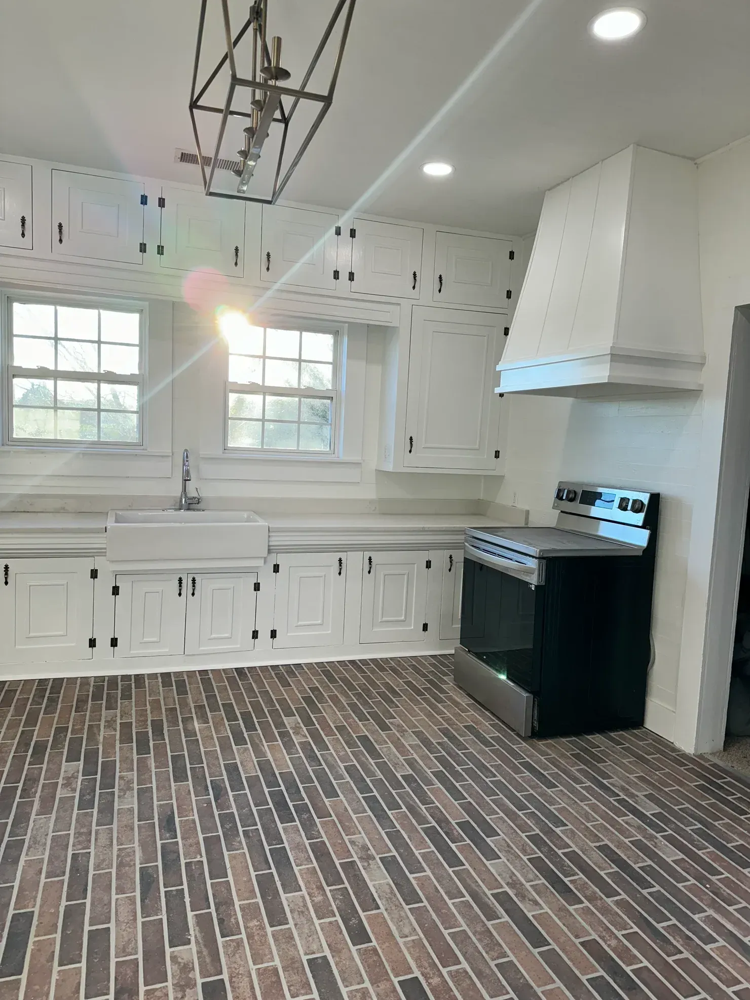 Bright kitchen with white cabinets, brick floor, windows, and a black stove by the range hood.