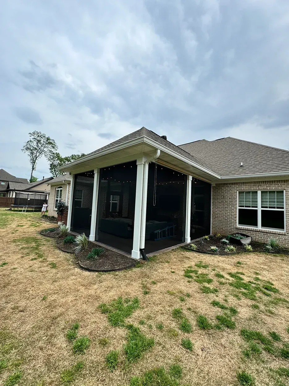 Damaged single-story house with a black porch and patchy dry yard under a cloudy sky