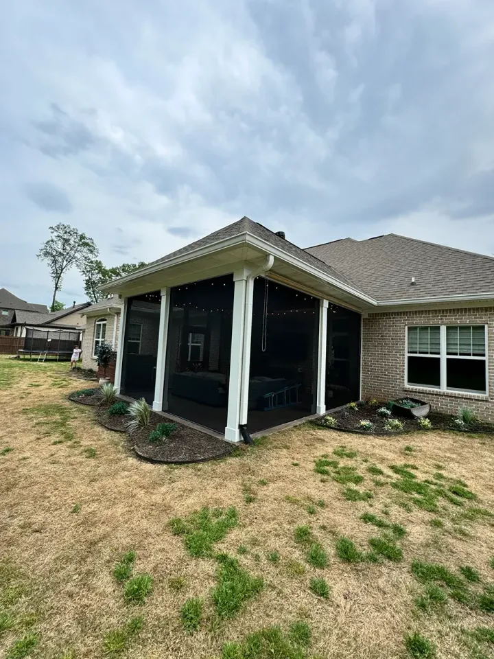Damaged single-story house with a black porch and patchy dry yard under a cloudy sky