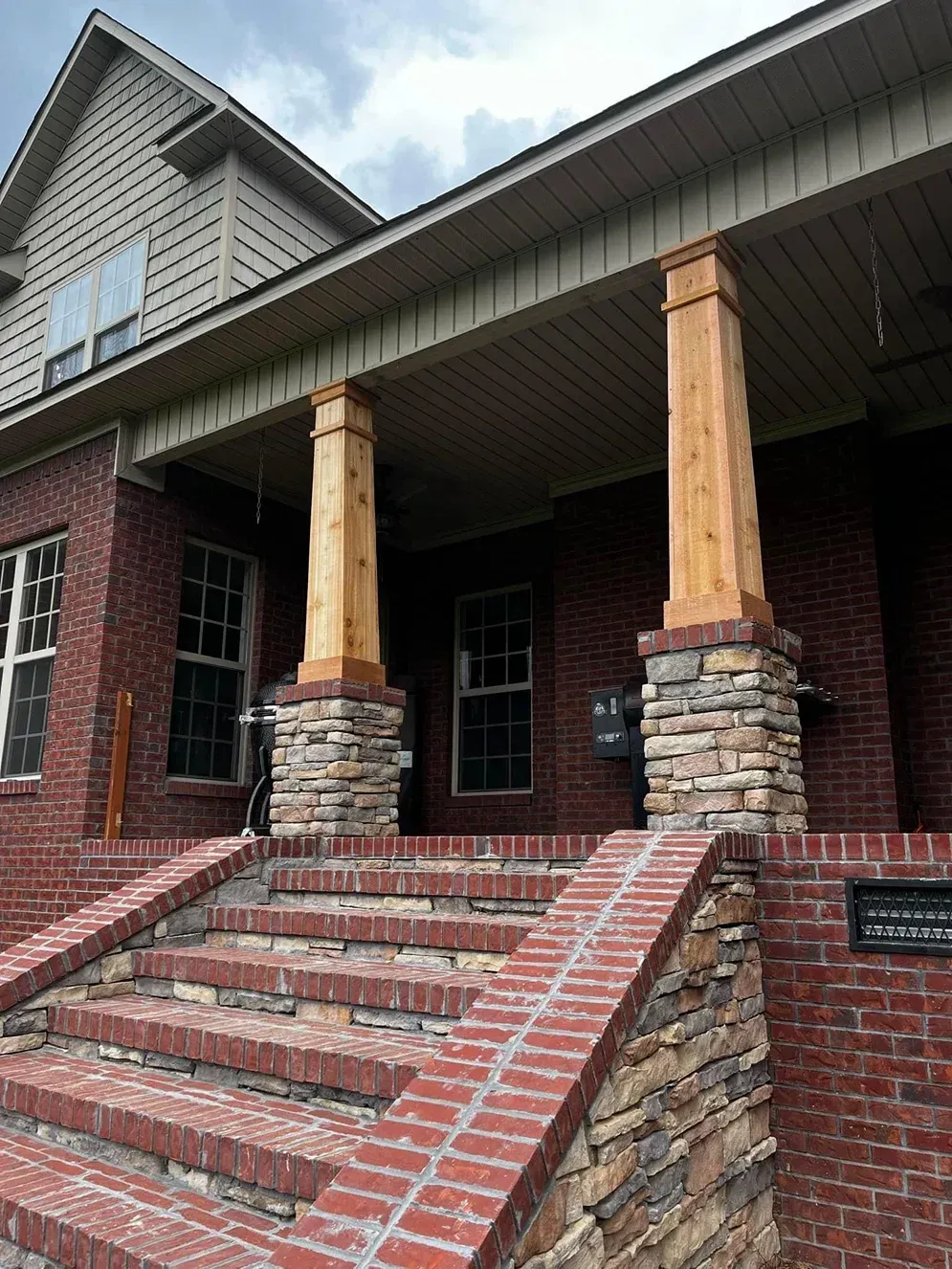 Brick front porch with stone steps, wooden columns, and a gabled roof on a house.