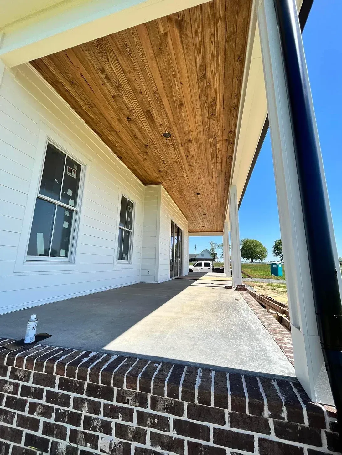 Covered porch with white siding, wood ceiling, brick steps, and a view toward the yard and driveway