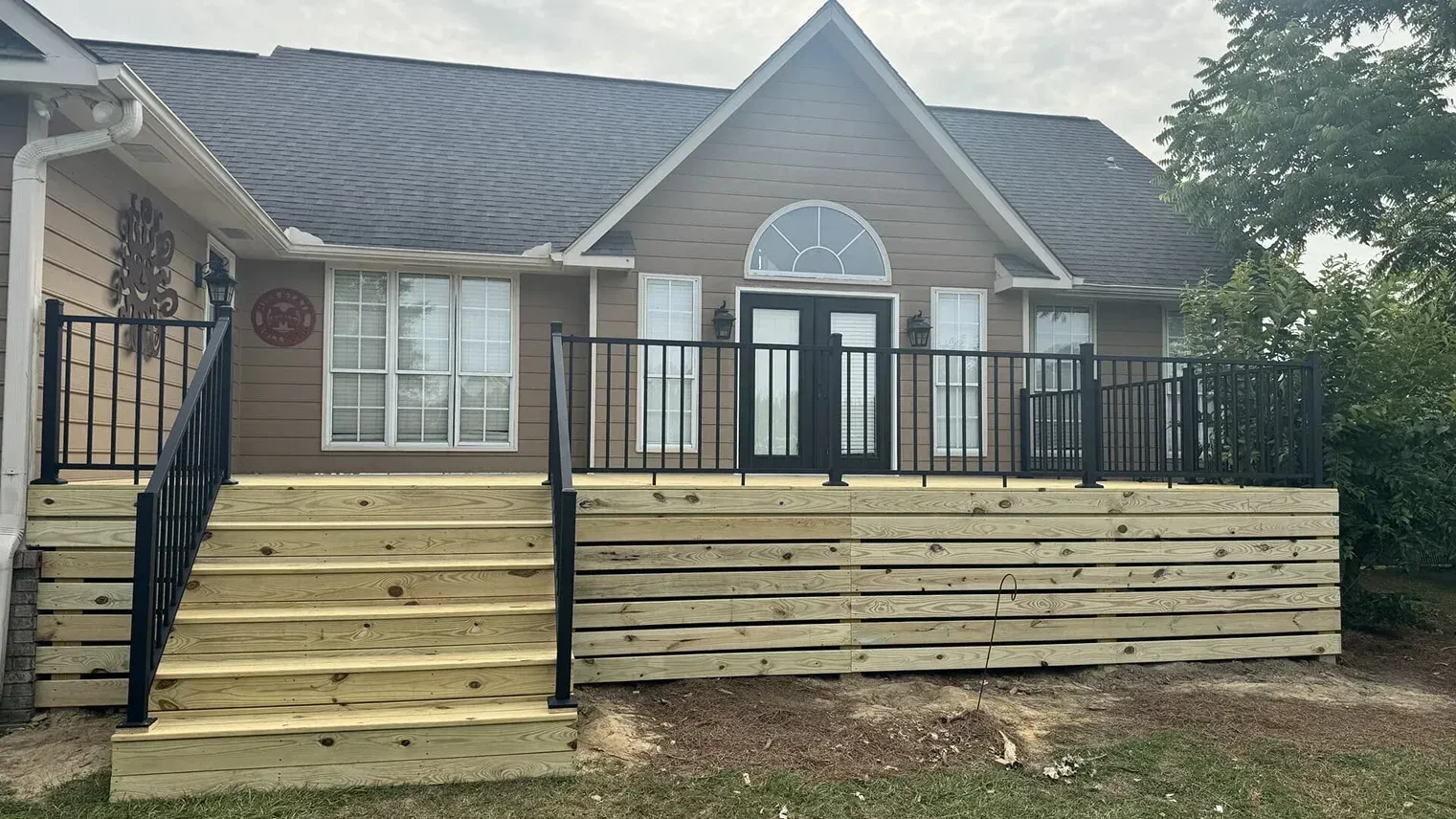 Front porch with wooden steps, black railings, and a house entry with arched window and double doors