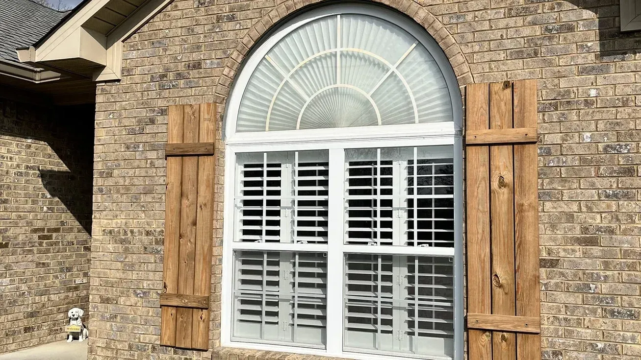 Stone house exterior with arched window, white shutters, and wooden shutters on either side
