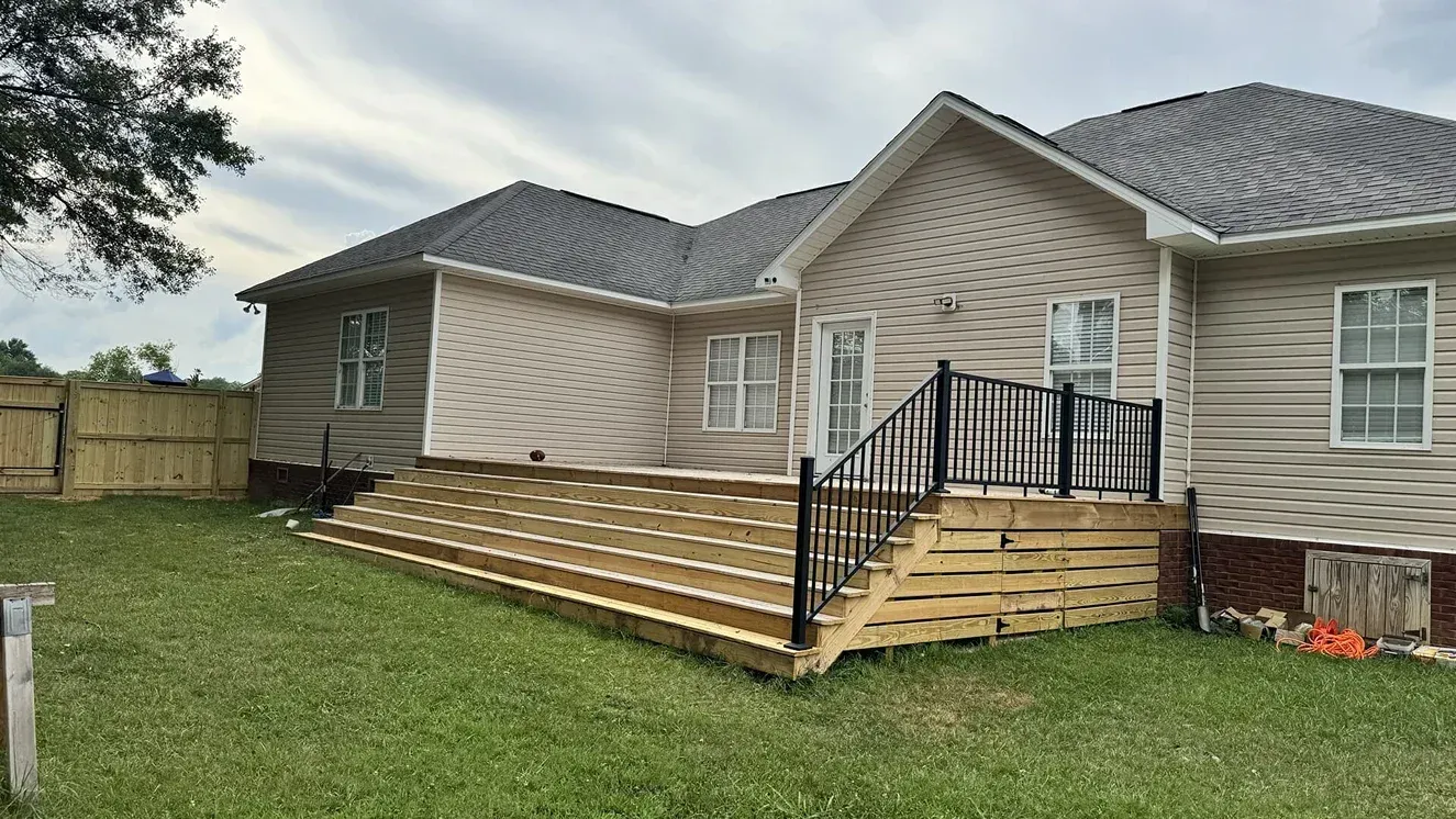 New wooden front steps and ramp added to a beige house with a black railing and green lawn