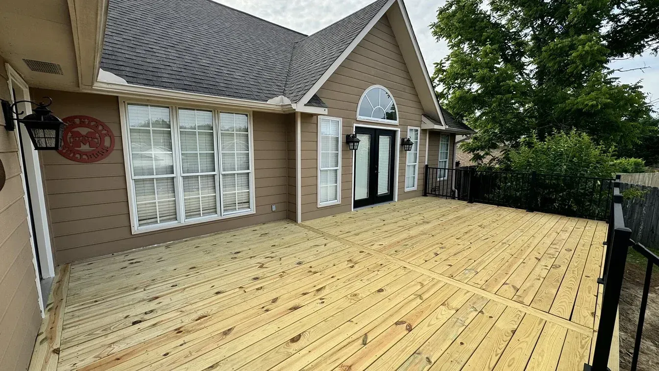 New wooden deck beside a tan house with white trim and black-framed doors