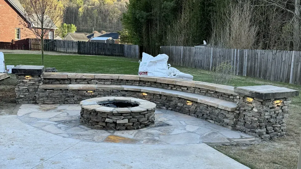 Backyard stone fire pit with curved seating wall, patio, and snow in the yard.