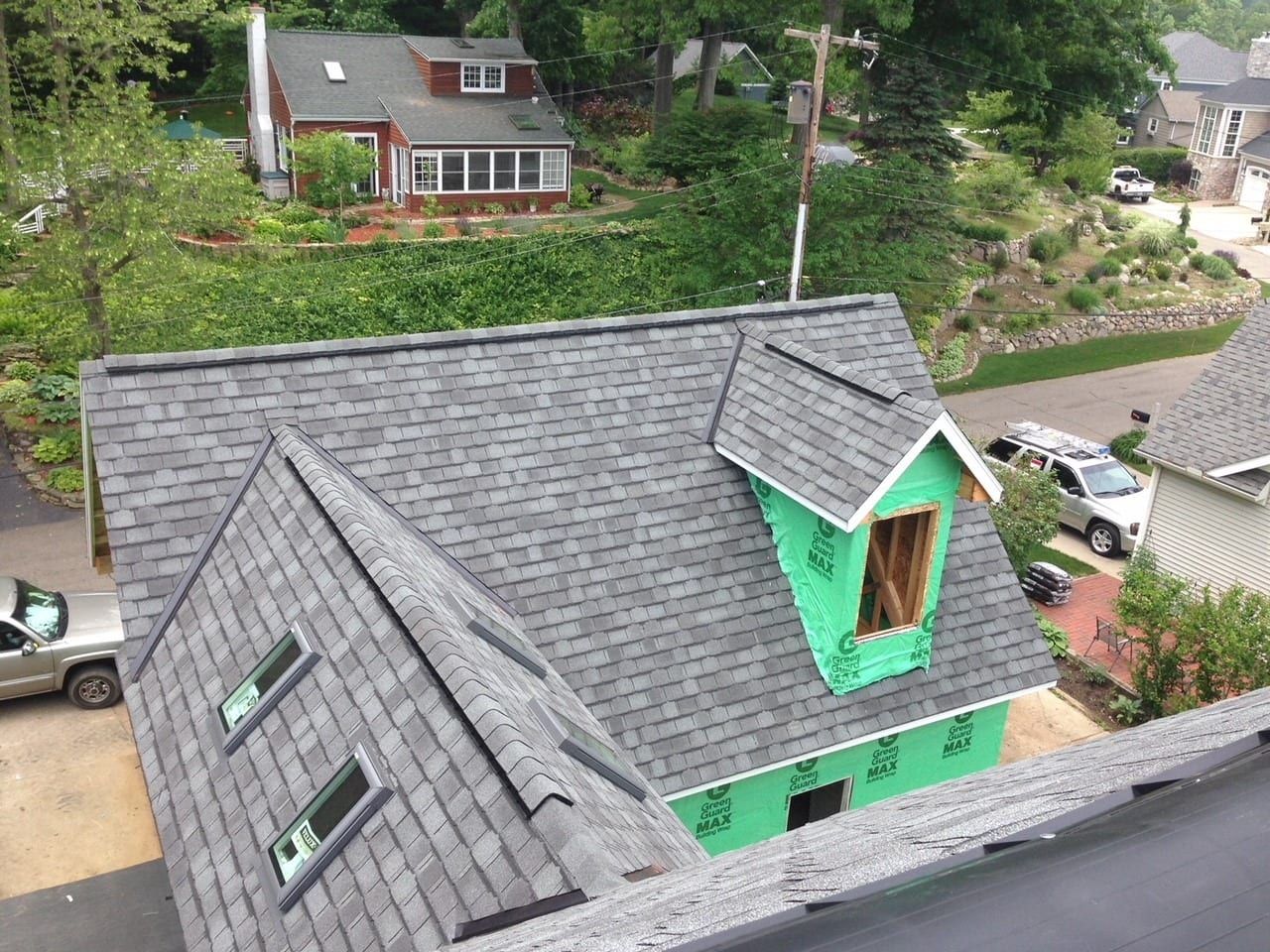 An overhead view of a gray shingled roof under construction with a green-sheathed dormer and two skylights.