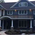 A two-story blue house with a covered front porch, dark metal roof, white trim, and a small garden in the front.