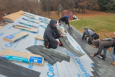 Four workers install shingles on a residential roof covered in protective underlayment.