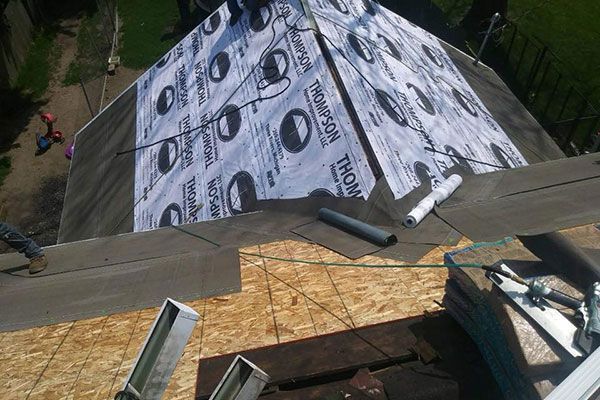 A high-angle view of a roof under construction, showing plywood sheathing and rolls of Thompson roofing underlayment.